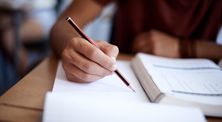 Closeup shot of a young man writing on a note pad