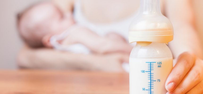 Mother holding a baby bottle with breast milk for breastfeeding at foreground, mothers breast milk is the most healthy food for newborn baby